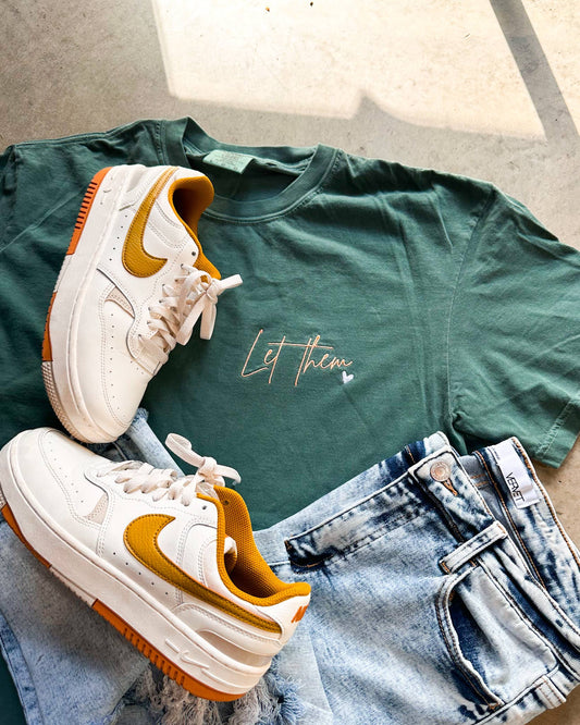 Green t-shirt with text, white and yellow sneakers, and blue jeans on a light wooden surface.