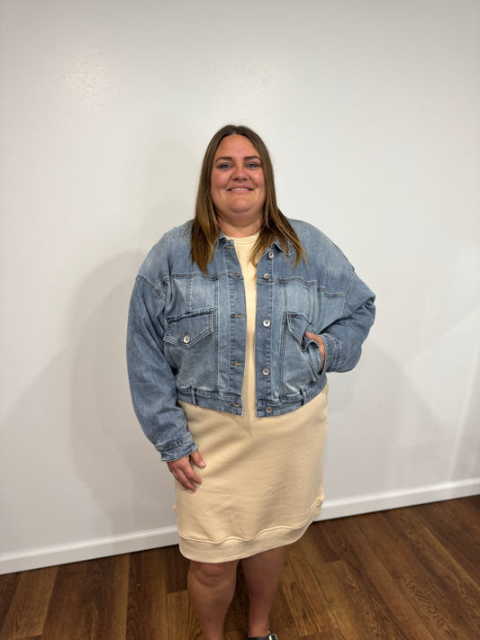 Person wearing a denim jacket and beige dress against a white wall.