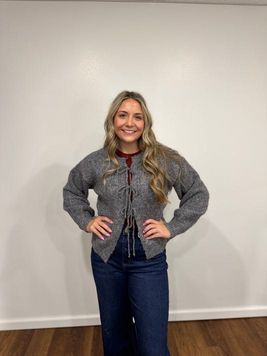 Woman wearing a gray tie cardigan with a white wall background