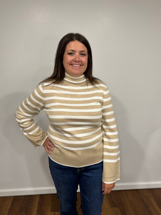 Woman wearing a striped turtleneck sweater and jeans against a plain wall.