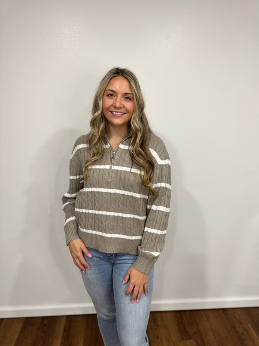 Woman wearing a striped sweater and jeans against a plain wall.