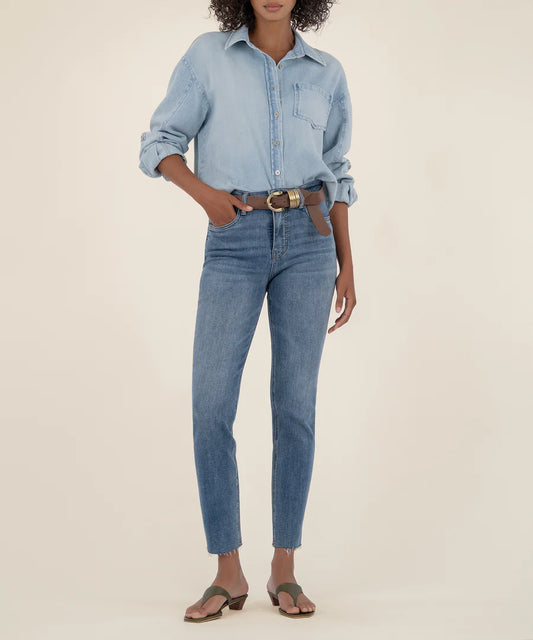 Person wearing a light blue denim shirt and jeans on a beige background