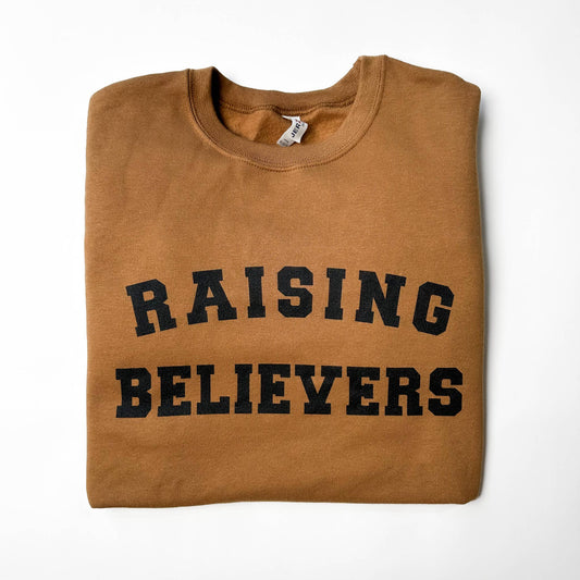 Folded brown sweatshirt with 'RAISING BELIEVERS' text on a white background