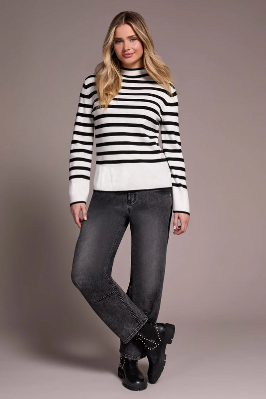 Woman wearing a black and white striped sweater and dark jeans against a plain background